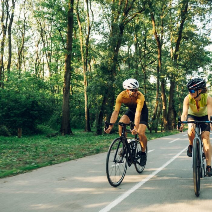 Two cyclists riding a tree-lined path, the forward-leaning position that makes cycling one of the easier spinal stenosis exercises