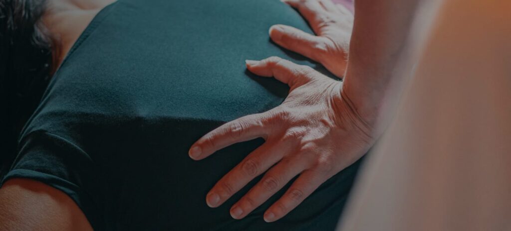 Therapist resting flat, light hands on a clothed back, the light contact used in manual lymph drainage
