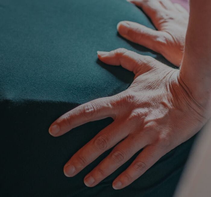Therapist resting flat, light hands on a clothed back, the light contact used in manual lymph drainage
